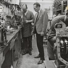 Three men repairing a slot machine in Mint Hotel's repair room with tools and parts on a table. (Black and white photo, 1960-1980)