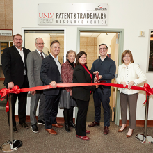 Zach Miles, Chris Heavey, Bo Bernhard, Jeanne Price, Betsy Fretwell, Steve Koziol, and Maggie Farrell pose in front of large red ribbon